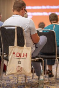 Im Vordergrund: DLH-Tasche mit Smiley - am Stuhl eines Zuhörers beim Vortrag von PD Dr. Gregor Hörmann, München, "KI in der Hämatologie". Im Vordergrund: DLH-Tasche mit Smiley - am Stuhl eines Zuhörers beim Vortrag von PD Dr. Gregor Hörmann, München, "KI in der Hämatologie".